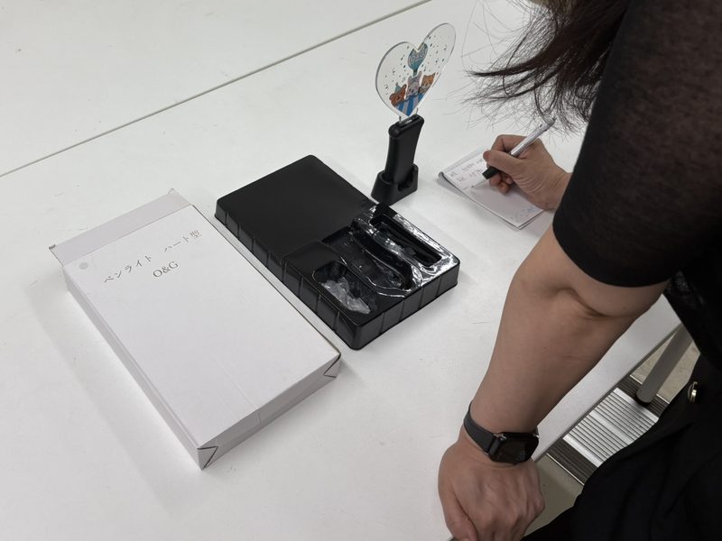 自社企画商品の現物とパッケージを机に置き、仕様をメモしている手元